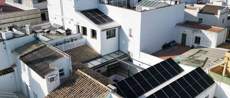 A rooftop with solar panels, a swimming pool, and multiple buildings with white walls and red-tiled roofs.