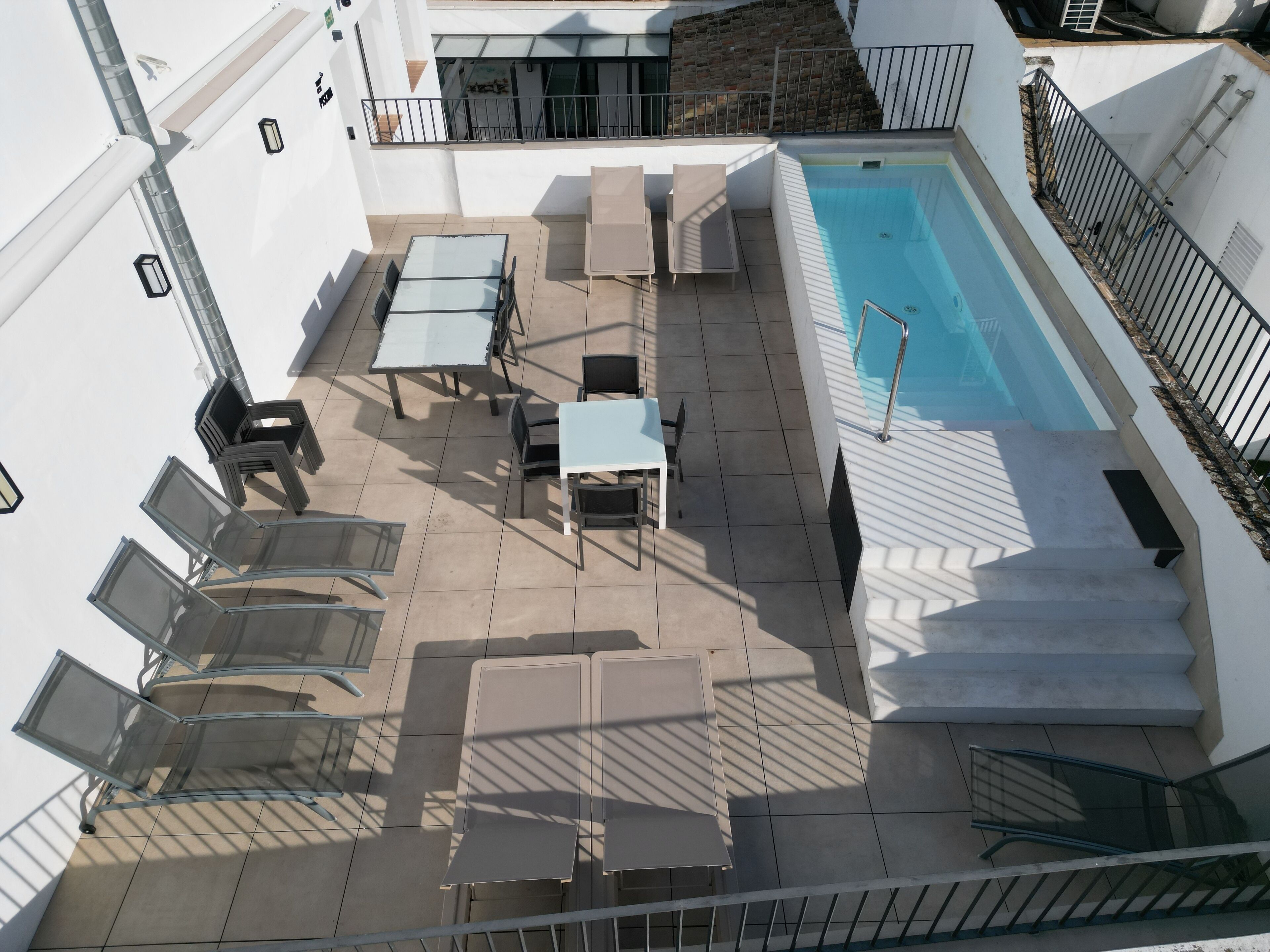 A rooftop pool area with outdoor seating and a staircase leading to a balcony.