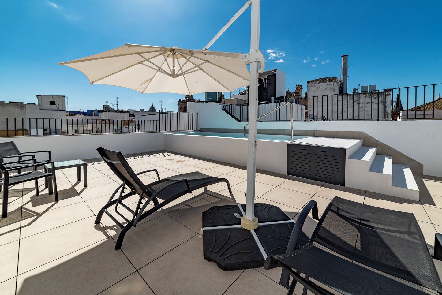 Eine Dachterrasse mit Pool, Liegestühlen und einem großen Sonnenschirm.