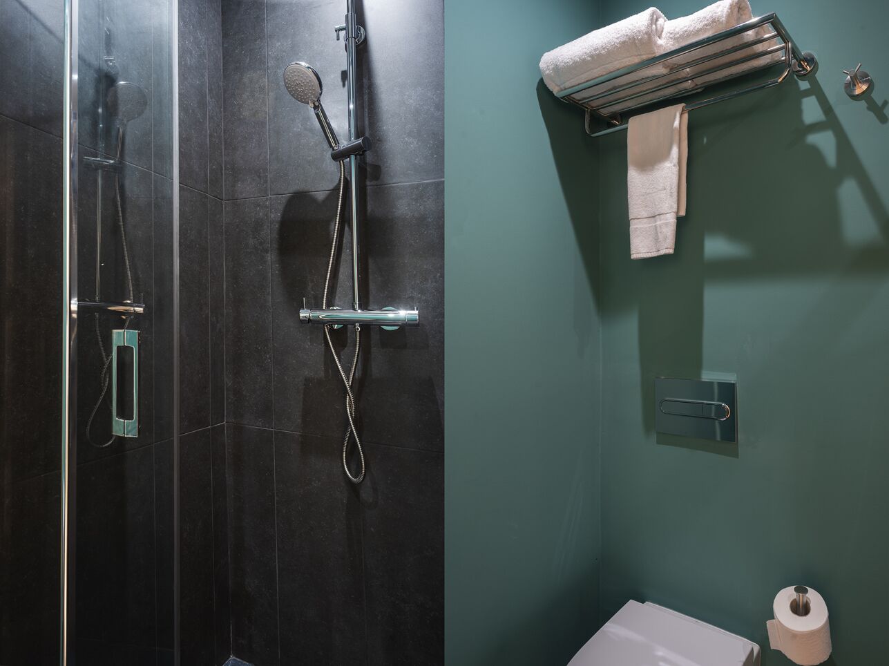 A bathroom with a shower, a towel rack, a toilet, and a toilet paper holder.