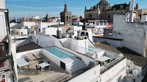 A rooftop terrace with a swimming pool, outdoor seating, and a view of historic buildings. - Slow Suites Salvador (Seville)