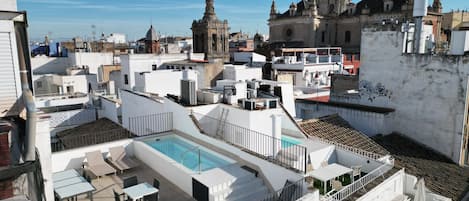 Eine Dachterrasse mit Pool, Sitzgelegenheiten im Freien und Blick auf historische Gebäude.