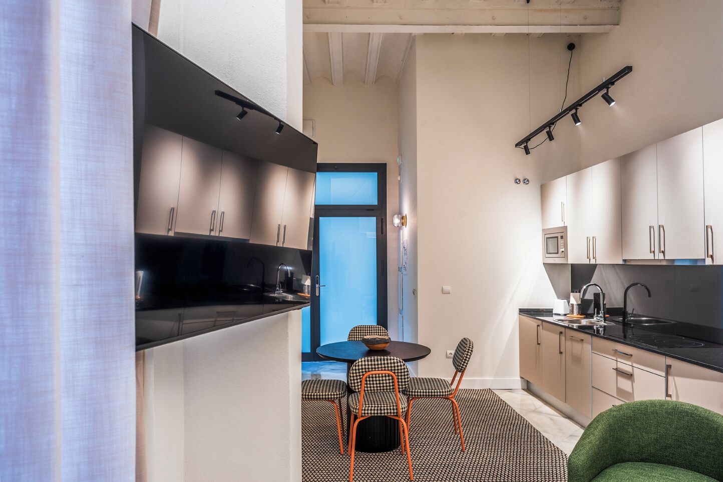 A modern kitchen with black countertops, a dining area with checkered chairs, and a green armchair.