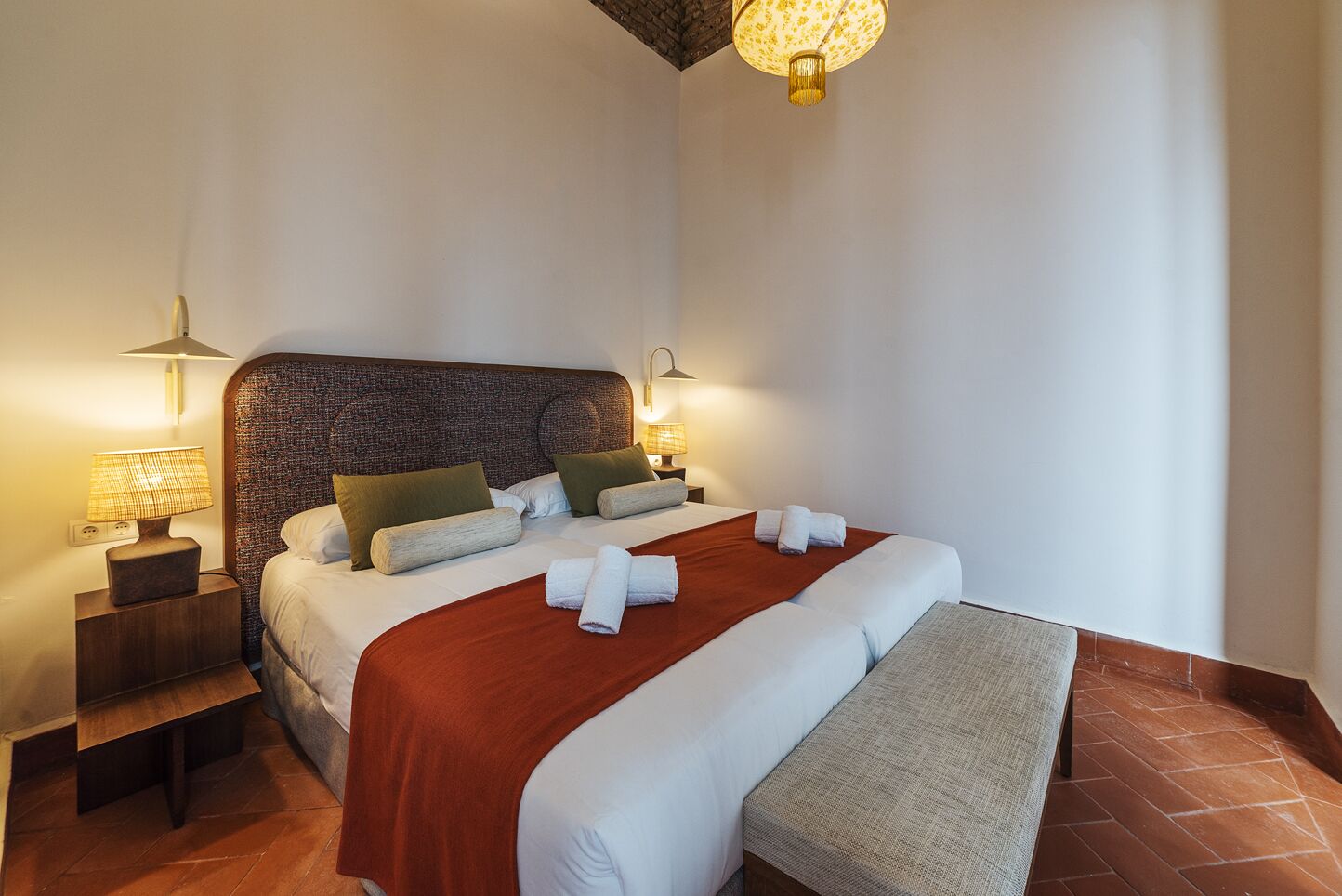 A neatly made bed with a red blanket, two bedside lamps, and a textured headboard.