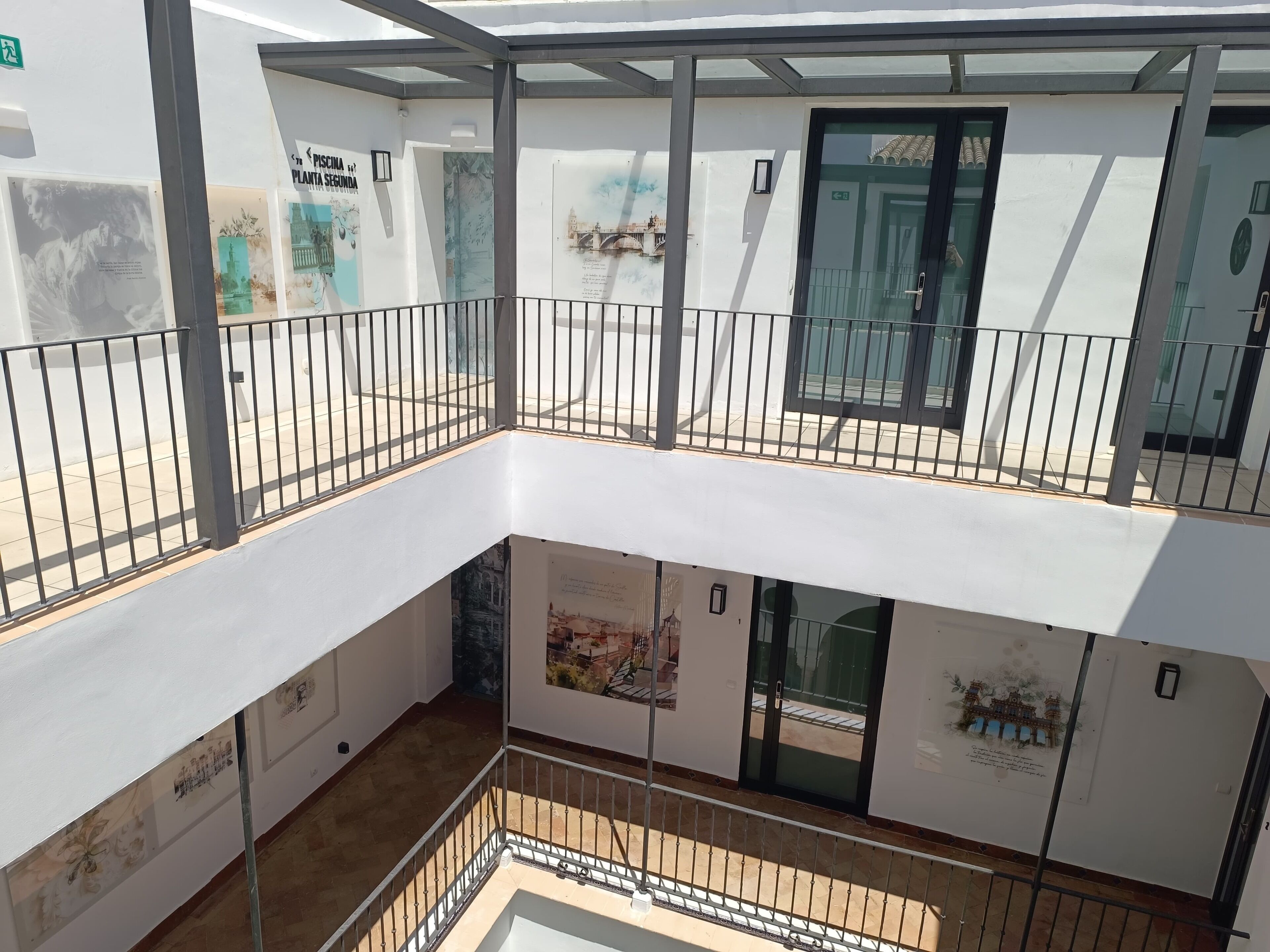 Een meerlaags atrium met glazen dak, metalen balustrades en kunstwerken aan de wanden.