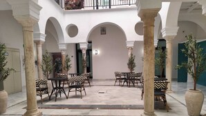 A spacious courtyard with marble flooring, surrounded by columns and featuring outdoor seating with patterned cushions. - Slow Suites Salvador (Seville)