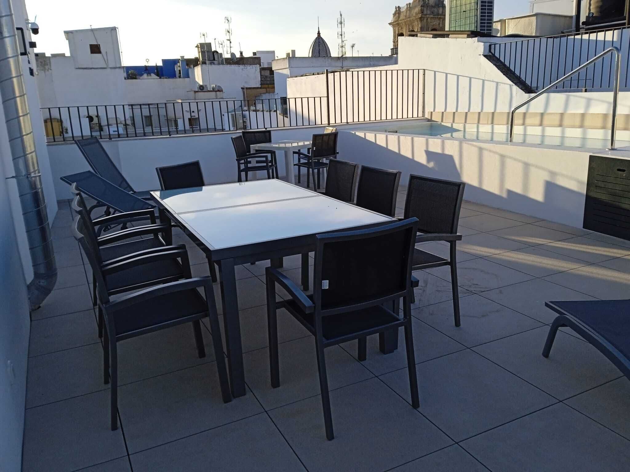 Una terrazza sul tetto con un tavolo rettangolare e sei sedie, circondata da una ringhiera in metallo.