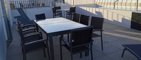 A rooftop terrace with a rectangular table and six chairs, surrounded by a metal railing.