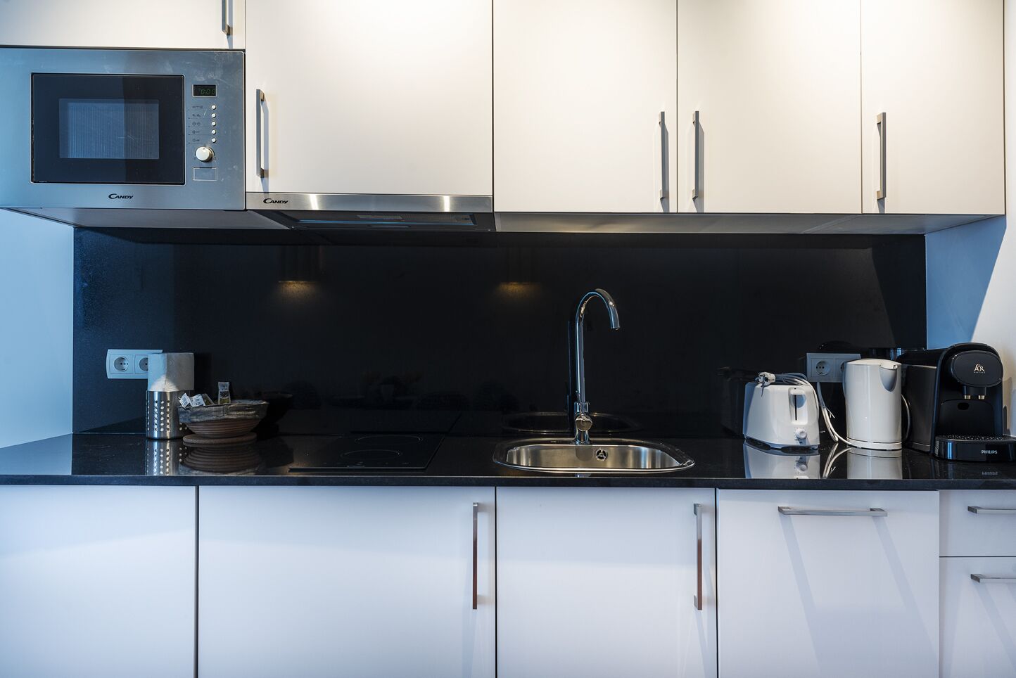 A modern kitchen with white cabinets, a stainless steel sink, a microwave, and a coffee maker.