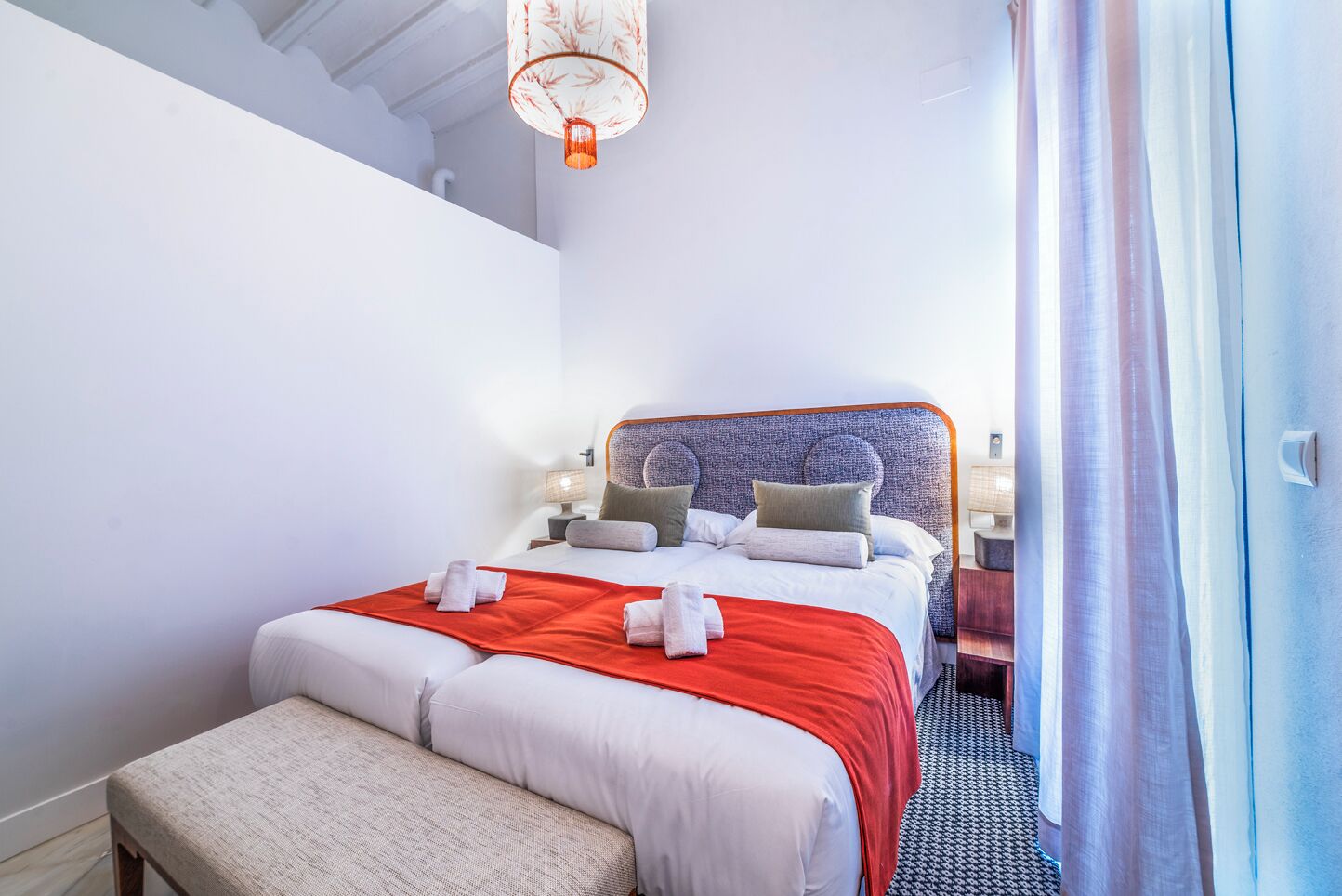 Une chambre d’hôtel avec un grand lit, une banquette, une table de chevet et une lampe suspendue.