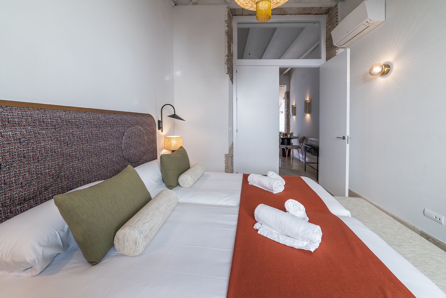 Une chambre d’hôtel avec un lit, une couverture rouge et une tête de lit à motifs texturés.