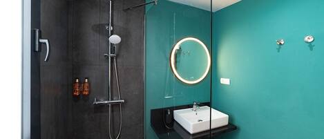 A modern bathroom with a dark shower, a white sink, a round mirror, and a teal wall.