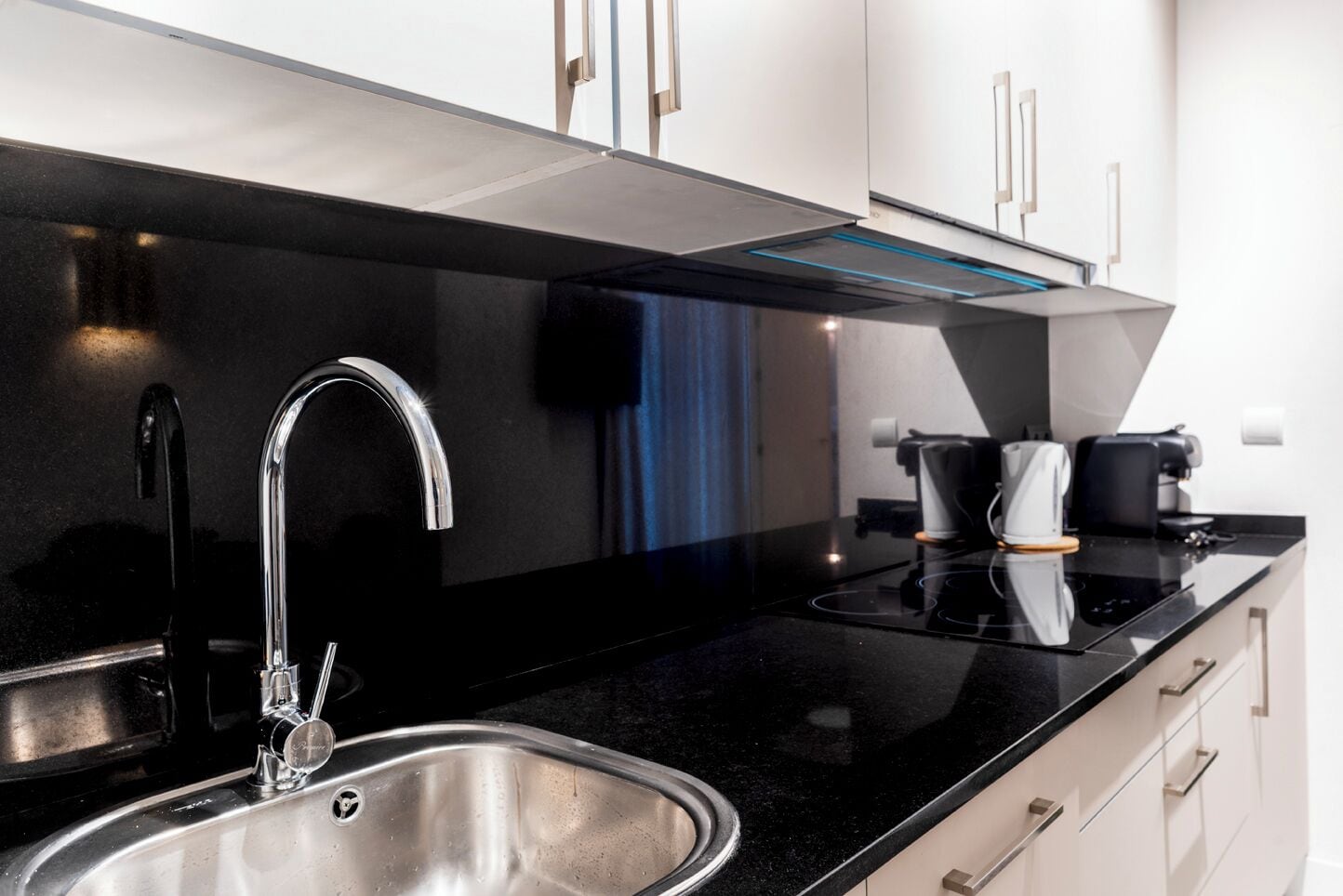 A modern kitchen with a stainless steel sink, black countertop, and white cabinets.