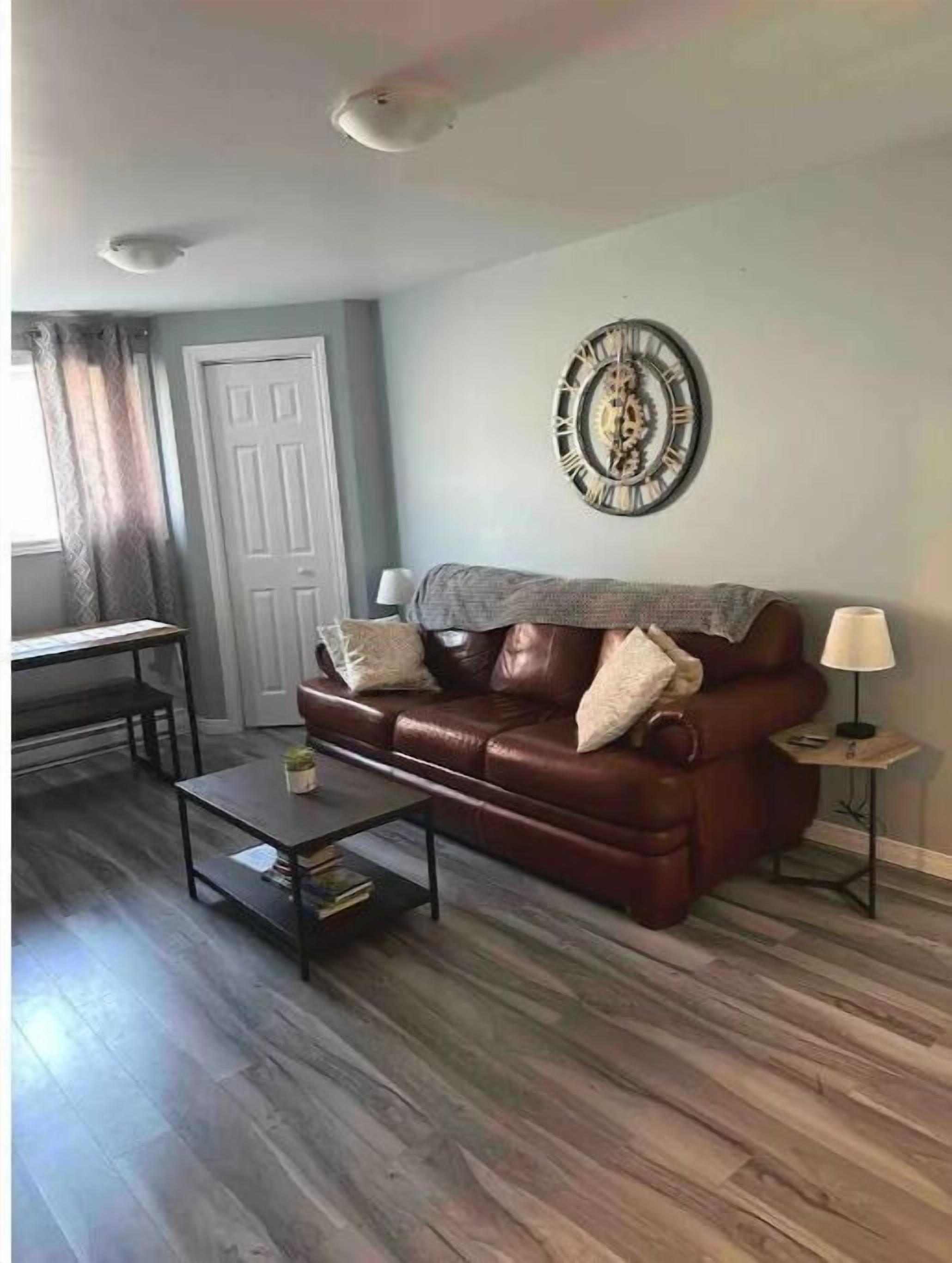A living room with a brown leather sofa, a coffee table, a wall clock, and a lamp.
