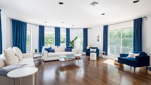 A spacious living room with a white sofa, blue armchairs, and a glass coffee table.