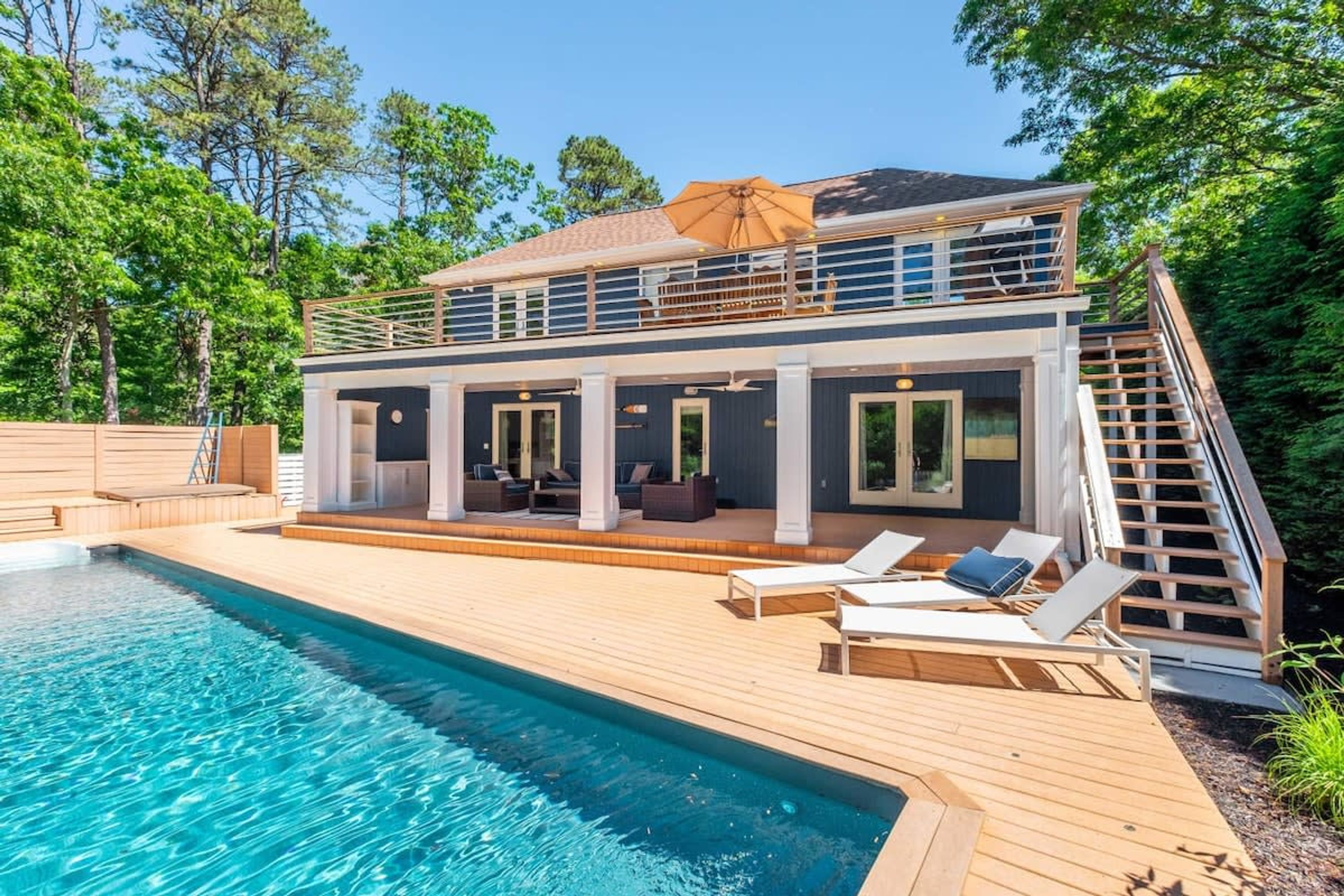 Uma casa de dois andares com piscina, área de estar externa e escadaria que leva a uma varanda.