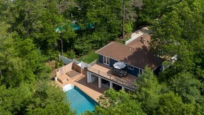 An aerial view of a house with a swimming pool, surrounded by dense trees.
