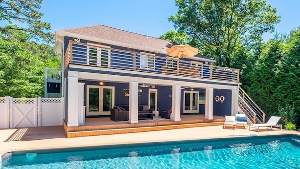 A two-story house with a pool, featuring a covered patio, outdoor seating, and a staircase leading to the upper level.