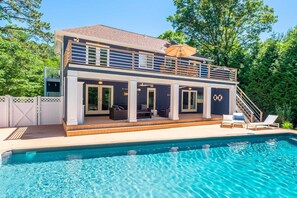 Et toetagers hus med swimmingpool, med en overdækket terrasse, udendørs møbler og en trappe til øvre plan.