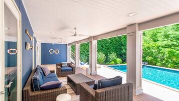 Espaço coberto ao ar livre com móveis de vime, piscina e vista para o verde.
