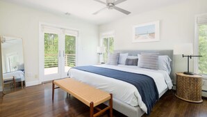 A bedroom with a large bed, a ceiling fan, a bench, and a round side table.