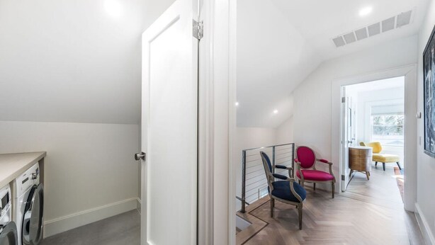 A modern interior with a laundry area, a staircase, and a seating area with colorful chairs. - Heated Pool Grill Breakwater by Rovetravel (Sag Harbor)