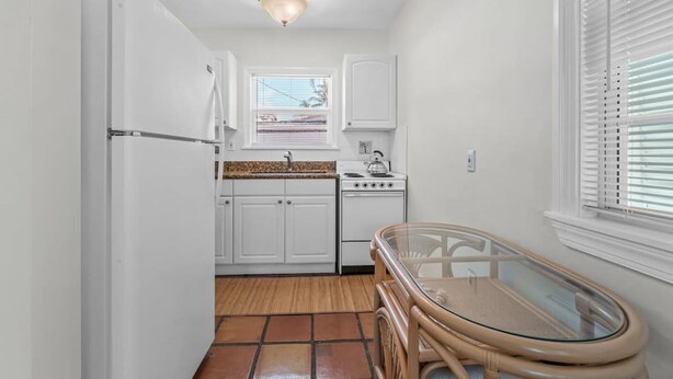 A compact kitchen with white cabinets, a stove, and a glass table. - Heated Pool Beach Miramar Villa by Rovetravel (West Palm Beach)