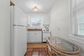 A compact kitchen with white cabinets, a stove, and a glass table. - Heated Pool Beach Miramar Villa by Rovetravel (West Palm Beach)