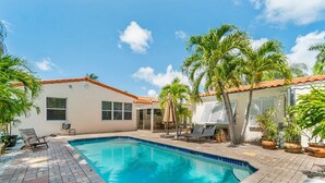 A swimming pool with a tiled deck, surrounded by palm trees and a building with a tiled roof. - Heated Pool Beach Miramar Villa by Rovetravel (West Palm Beach)