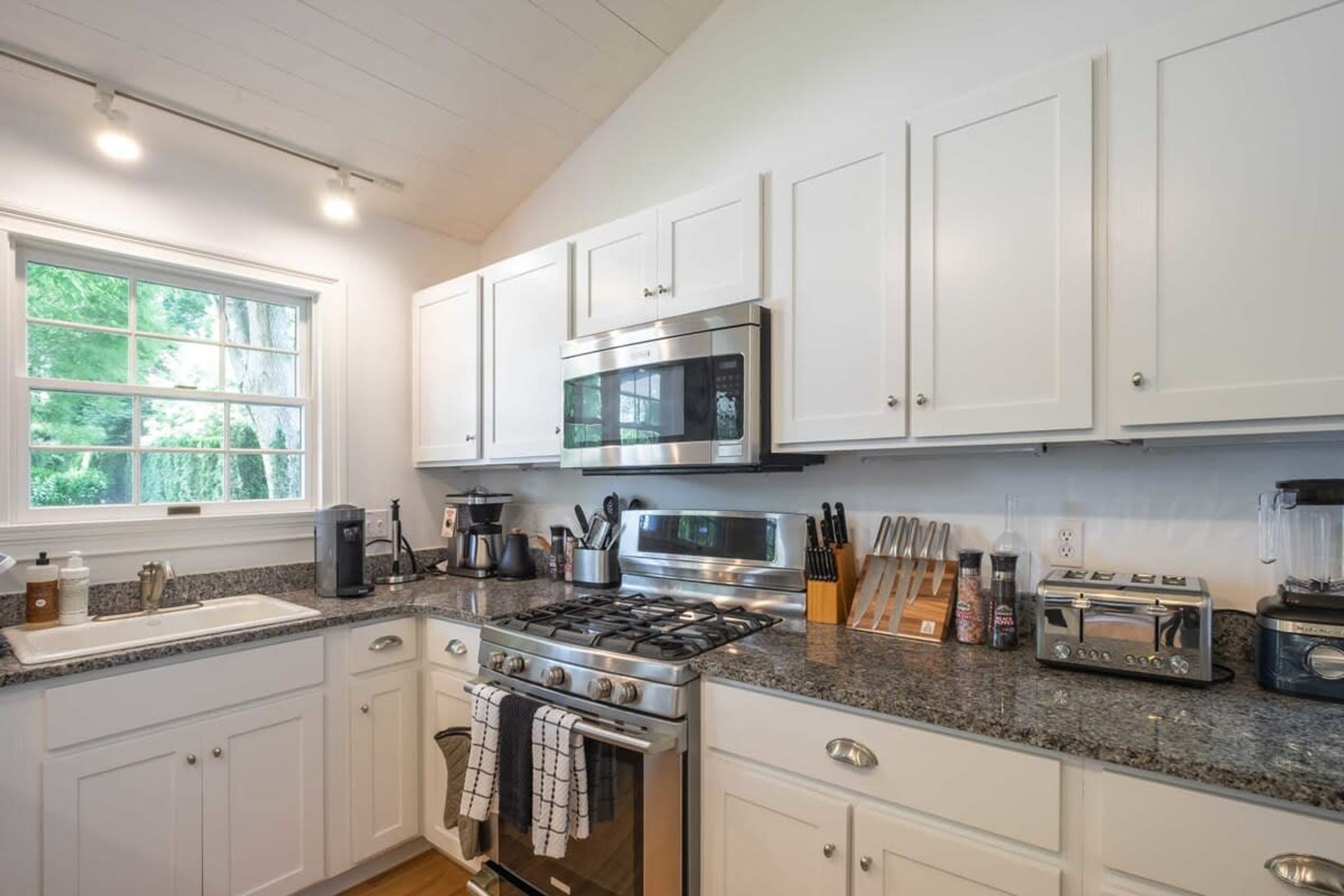 A modern kitchen with white cabinets, a gas stove, a microwave, and a toaster.
