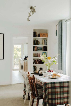 A dining area with a table set for two, a bookshelf, and a washing machine in the background.
