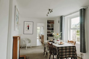 A dining area with a table set for four, a bookshelf, and a framed picture on the wall. - Frobisher Apartments (Falmouth)