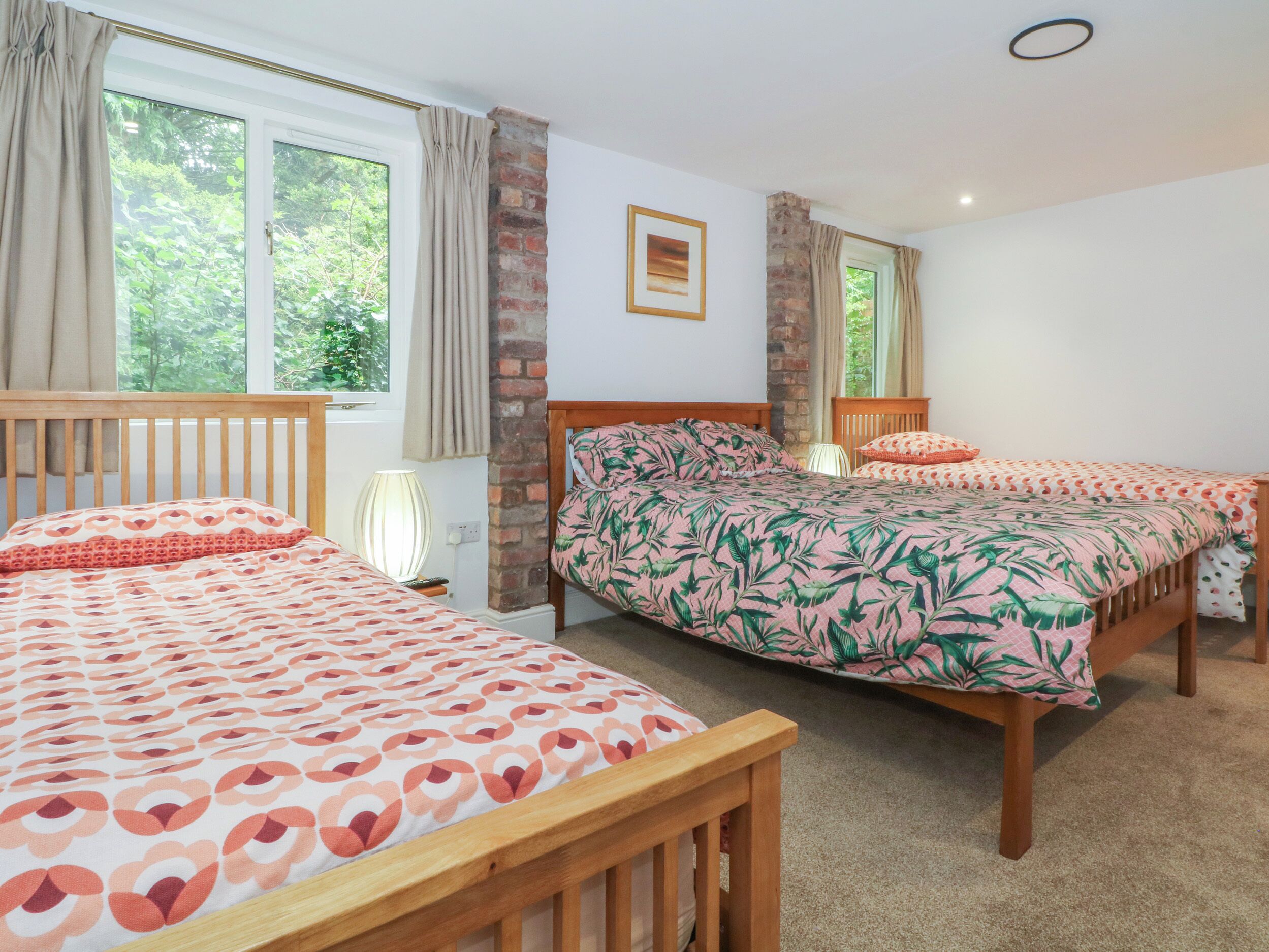A bedroom with two wooden beds, a brick wall, and a window with curtains.