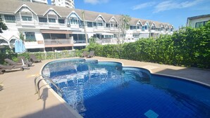 Une piscine avec des chaises longues et, au fond, un bâtiment doté de nombreux balcons.