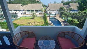 Un balcon avec des fauteuils en osier et une vue sur une piscine, des bâtiments et une colline.