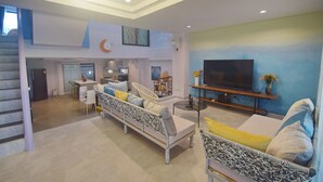 Un salon spacieux avec un canapé, des fauteuils, un téléviseur et un escalier.