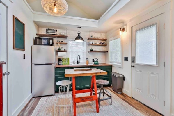 A compact kitchen with a refrigerator, microwave, and wooden table.