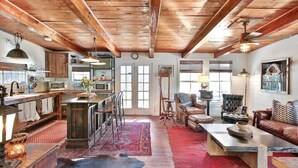 Un intérieur rustique avec des poutres apparentes, une cuisine équipée d’appareils modernes, un coin salon confortable avec des canapés en cuir et une moquette rouge.