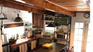 Une cuisine rustique avec des poutres en bois, un îlot central, des tabourets de bar et une poubelle.