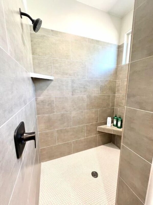 A shower with a handheld showerhead, a wall-mounted faucet, and a shelf with toiletries.