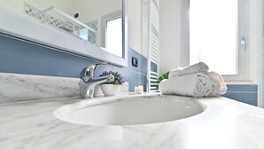 Un baño con lavamanos de mármol, un espejo, una toalla y un pequeño florero con flores.