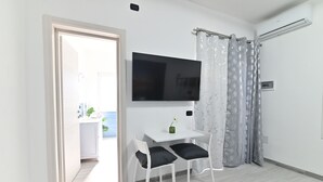 Habitación pequeña y moderna con una mesa blanca y dos sillas, un televisor de pantalla plana en la pared y una zona de ducha con cortina.