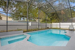 A swimming pool with a glass enclosure, surrounded by a concrete deck and a white wall. - Private Pool, 4 Miles to Disney-6BR / 4 baths Home (Kissimmee)