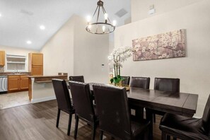 A dining area with a dark wooden table, six chairs, a chandelier, and a floral painting on the wall. - Private Pool, 4 Miles to Disney-6BR / 4 baths Home (Kissimmee)