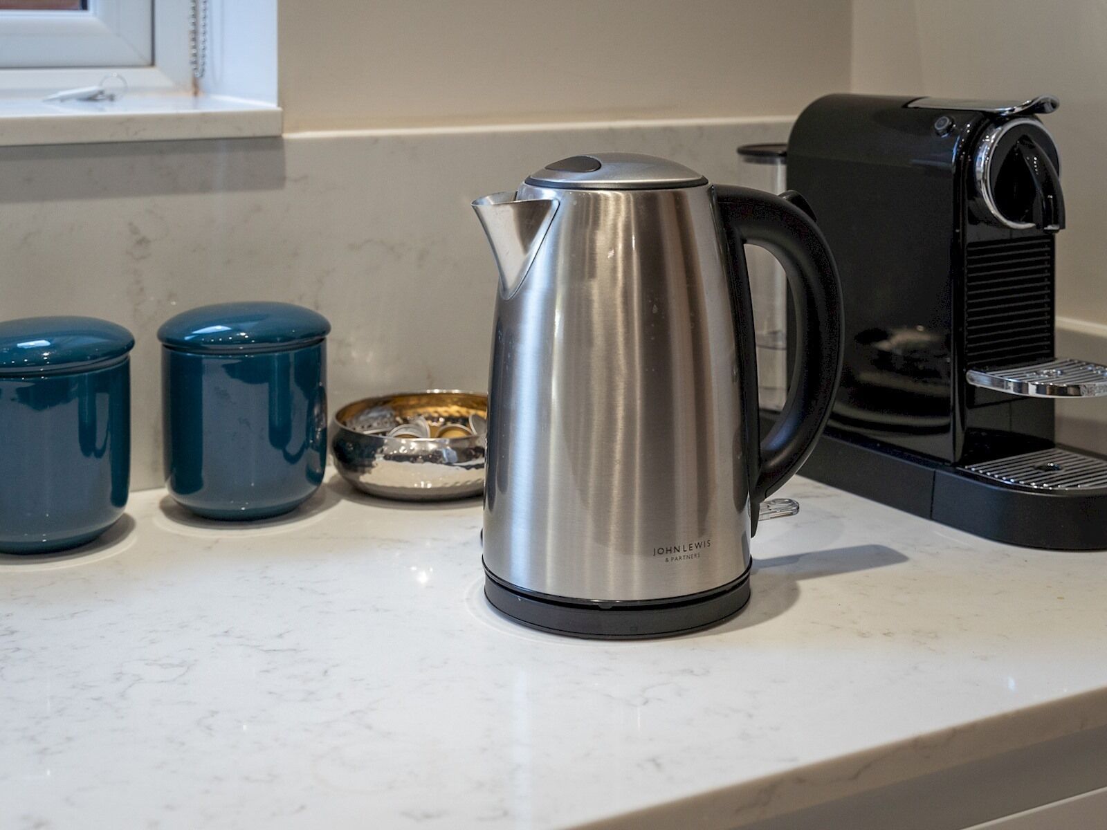 Un plan de travail de cuisine avec une bouilloire en acier inoxydable, une machine à café et deux récipients bleus.