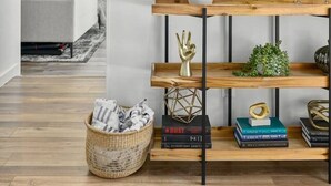 Ein modernes Wohnzimmer mit einem Holztischchen, das Bücher und Dekorationsgegenstände präsentiert, einer weißen Vase mit Grünpflanzen und einer Wand, die mit schwarz-weißen gerahmten Fotografien geschmückt ist.