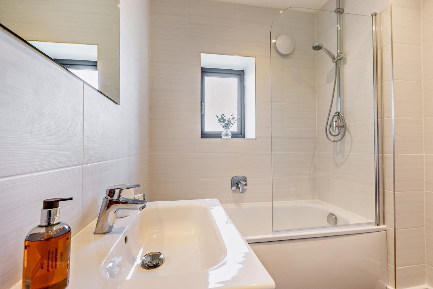 Une salle de bain moderne avec un grand lavabo blanc, une douche en verre et une petite fenêtre agrémentée d’une plante.