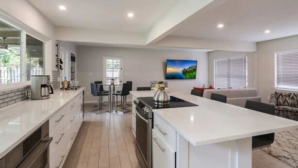 A modern kitchen with a central island, dining area, and a living space with a sofa and TV. - The Clematis - Entire house (Sarasota)