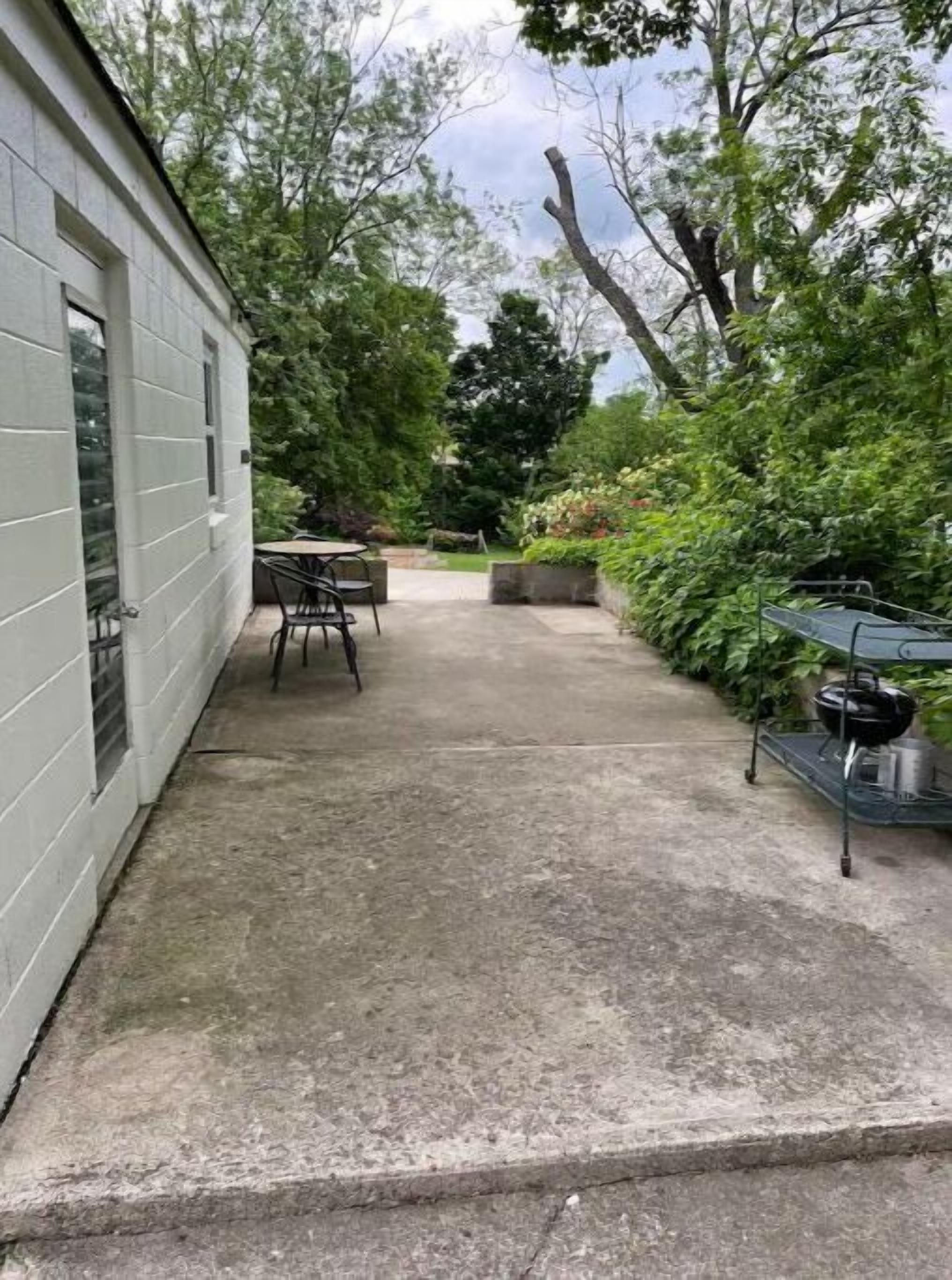 Ein überdachter Patio-Bereich mit Betonboden, einem Tisch, Stühlen und einem Grill.