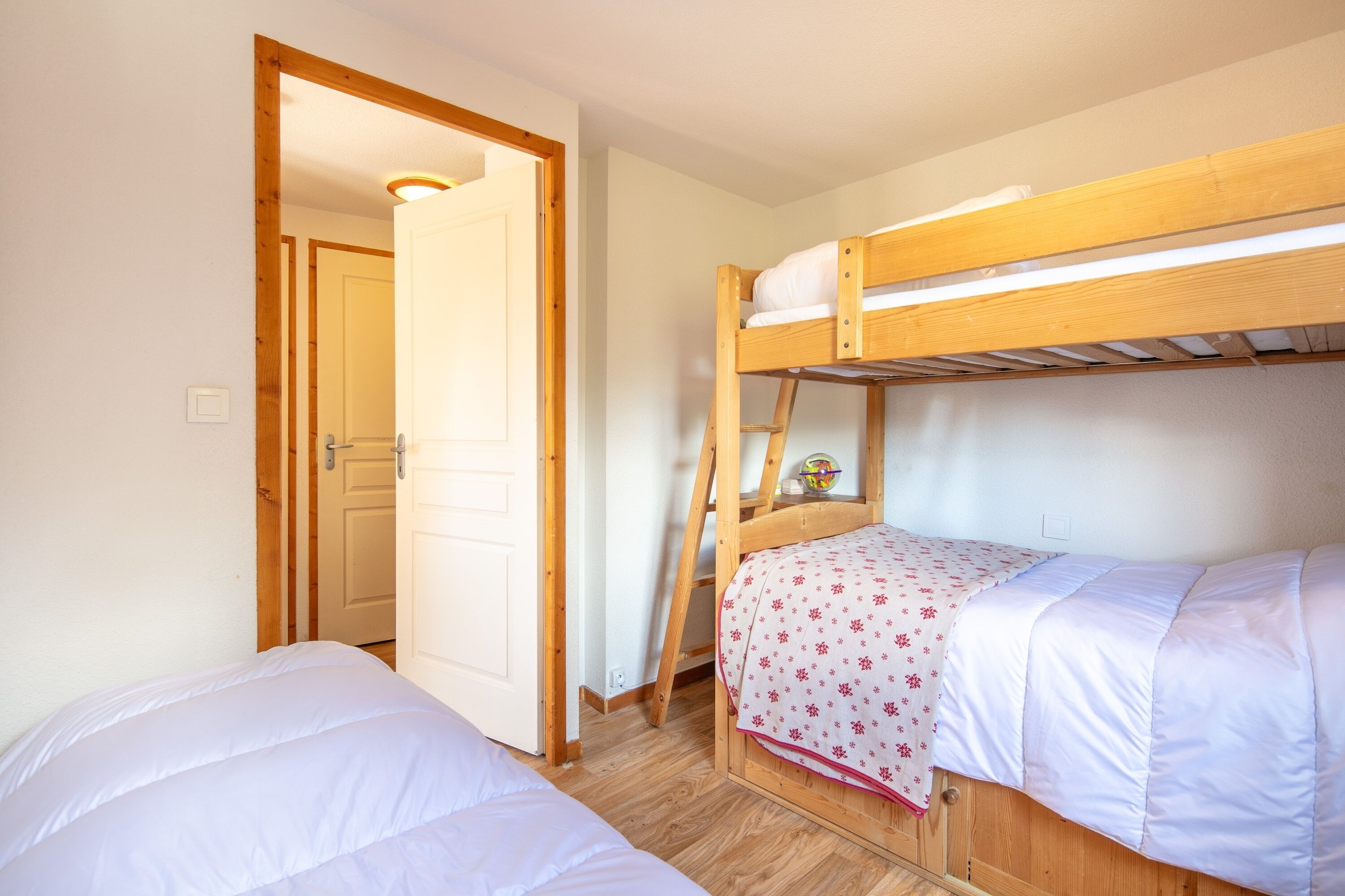 Une pièce avec deux lits superposés, des murs en bois, une porte et une petite étagère sur laquelle est posé un objet décoratif.